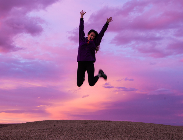 Smiling Woman Wearing Black Jacket and Pants Jumping in Brown Open Field